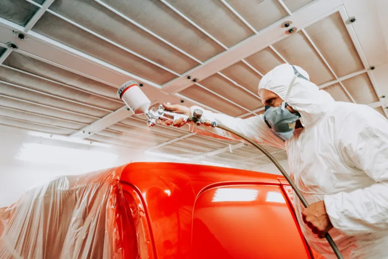 Automotive mechanical engineer painting the body of a red car with special suit